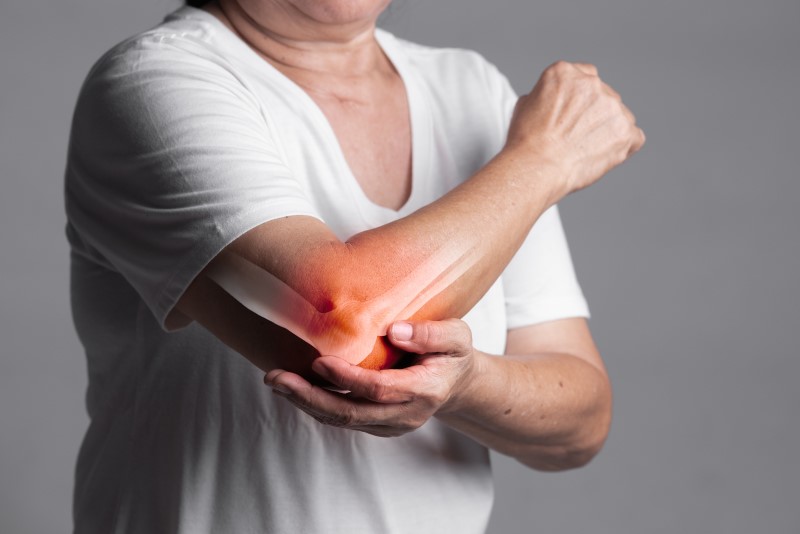 Osoba na zdjęciu trzyma się za łokieć, co może sugerować problem związany z łokciem golfisty. Łokieć golfisty to ból i zapalenie ścięgien wewnętrznej części łokcia, często spowodowane powtarzającymi się ruchami. Leczenie obejmuje odpoczynek, zimne okłady, ćwiczenia wzmacniające i, w razie potrzeby, fizjoterapię.