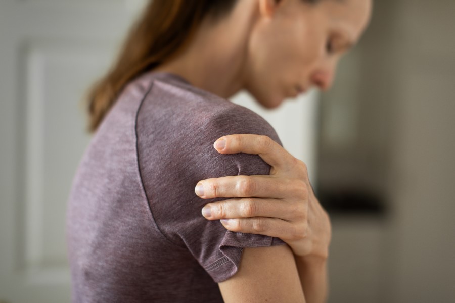 Obraz przedstawia osobę trzymającą się za ramię, co może sugerować problem związany z zapaleniem stawu barkowego.